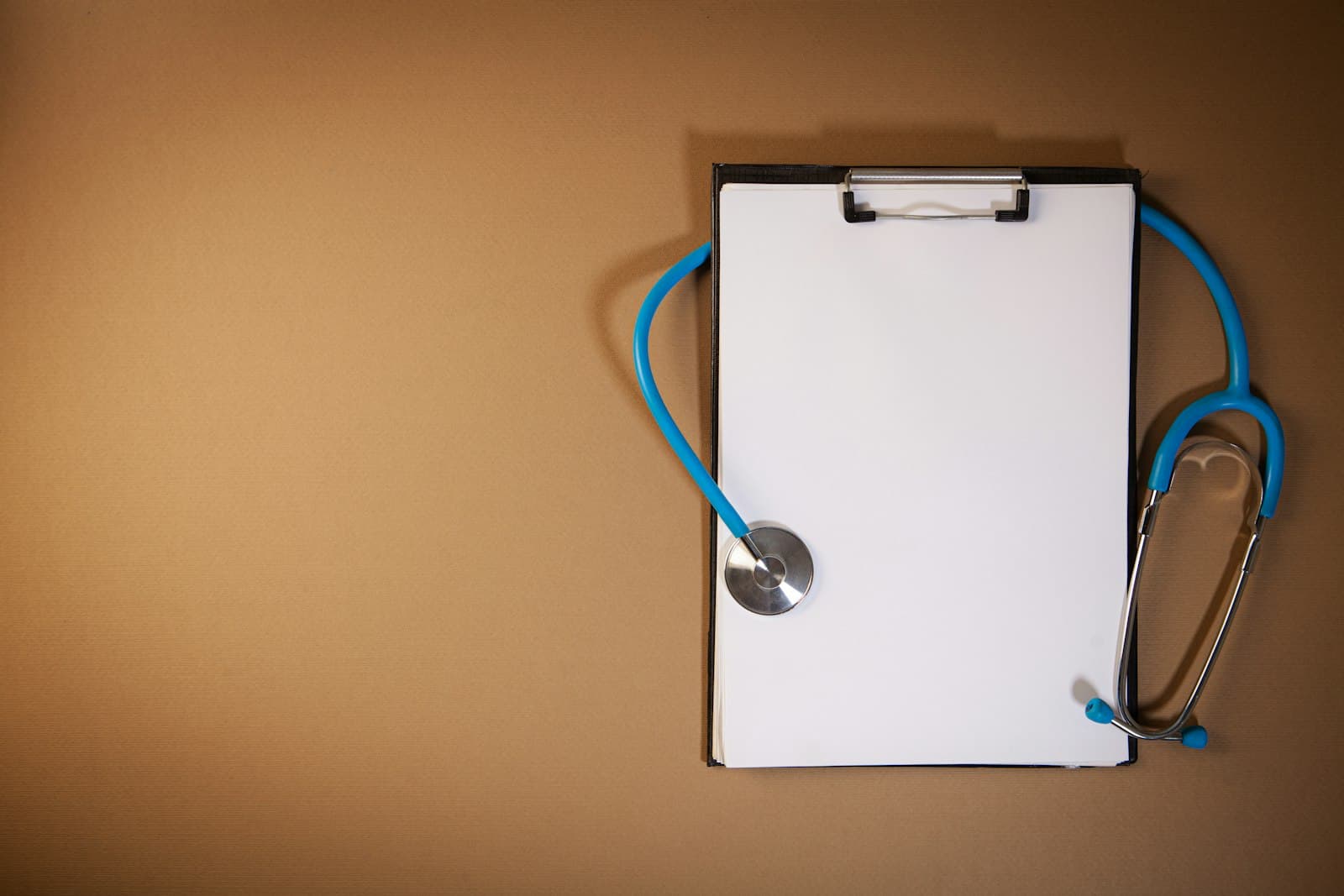 A clipboard and stethoscope on a plain brown background