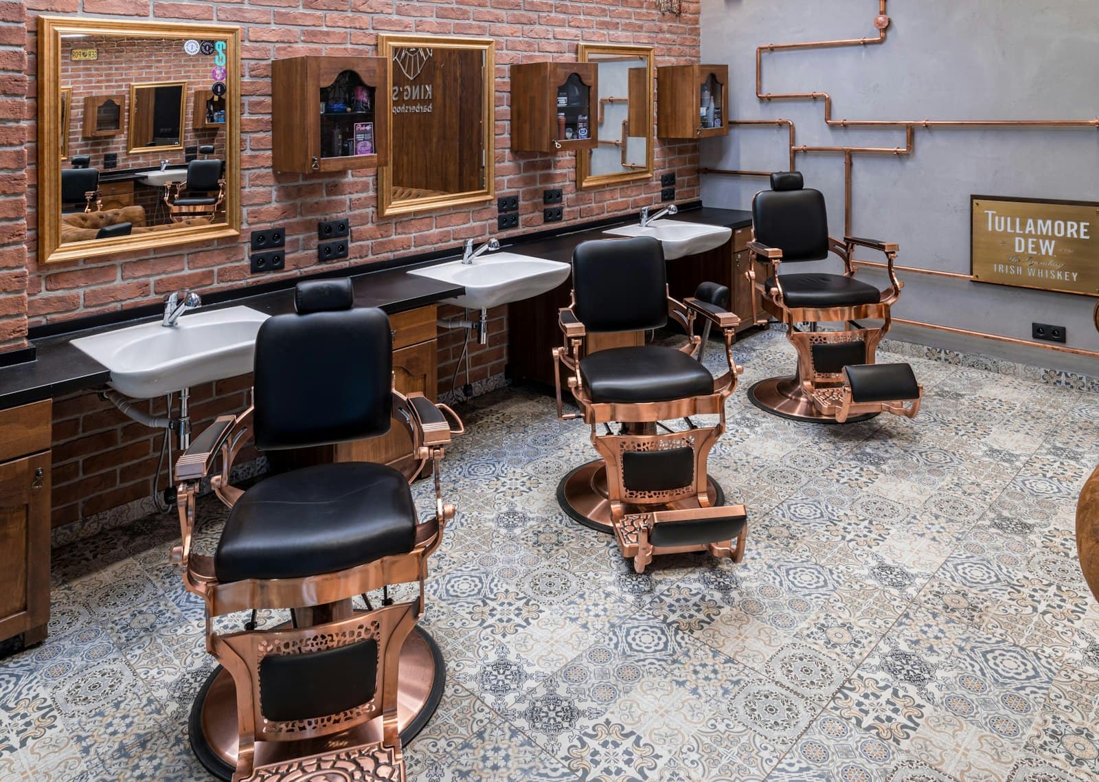 Copper and black barber chairs in front of mirrors on a brick wall